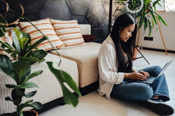 Portrait of woman working remotely from home using laptop computer while sitting on floor