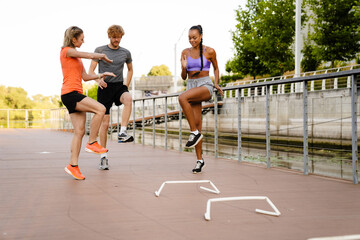 Group of three athletic people jumping during outdoor workout - obrazy, fototapety, plakaty