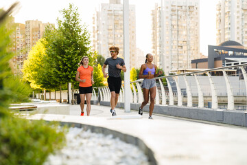 Group of three active people running together outdoors on bridge - obrazy, fototapety, plakaty