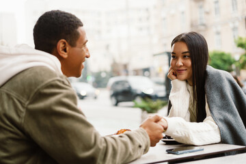 Smiling couple holding hands while sitting in cafe outdoors