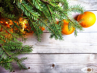 Festive decoration with bouquet and branches of spruce, bright glowing garlands, oranges on wooden background. Decor for Christmas and New Year. Abstract texture, frame, place for text, copy space