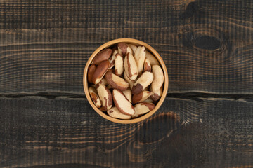 Peeled brazil nut in wooden cup on decorative wooden background
