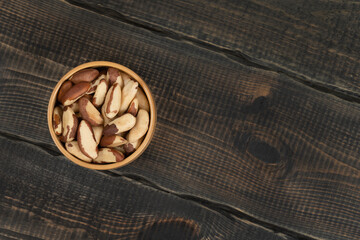 Peeled brazil nut in wooden cup on decorative wooden background