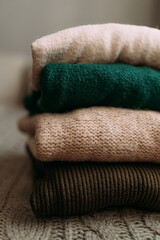 a stack of warm winter knitted wool sweaters in green and beige shades. A stack of women's sweaters is lying on the bed. What to wear in winter to keep warm