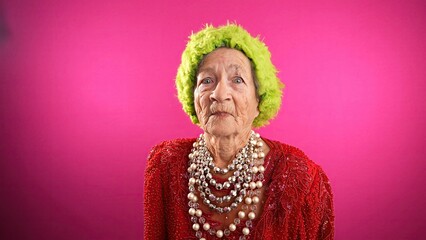 Displeased unhappy fisheye portrait caricature of funny elderly woman saying NO with green hat isolated on pink background.
