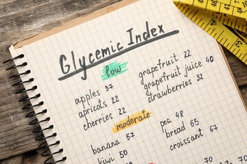 List with products of low and moderate glycemic index in notebook on wooden table, top view