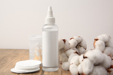 Composition with makeup remover and cotton flowers on wooden table against white background