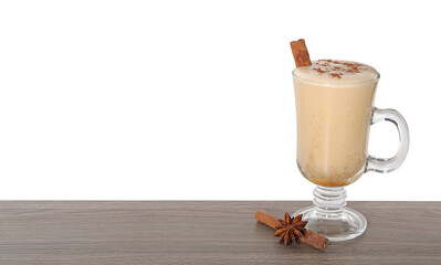 Delicious eggnog in glass, anise and cinnamon sticks on wooden table against white background,...