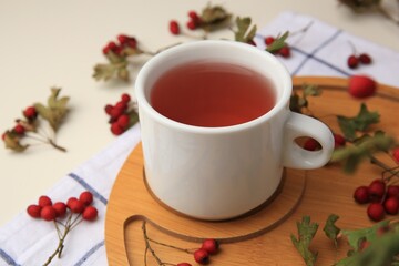Cup with hawthorn tea and berries on beige table, closeup