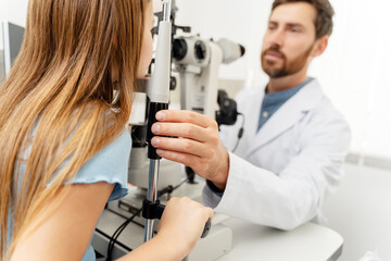 Male ophthalmologist using a binocular slit-lamp while checking the eyesight of girl