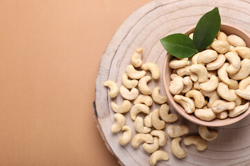 Tasty cashew nuts and green leaves on pale brown background, top view. Space for text