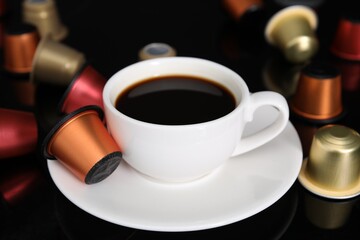 Obraz na płótnie Canvas Cup of coffee and capsules on black table, closeup
