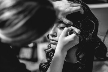 The beauty of preparation: a make-up artist getting a beautiful and young brunette model ready for...
