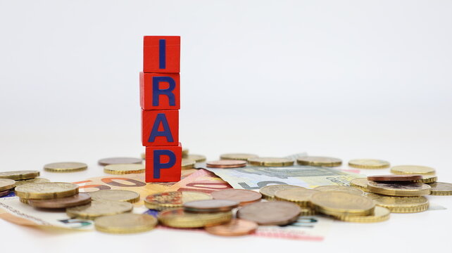 Singola parola "IRAP" su blocco di legno, tasse isolate, con sfondo di monete in euro.