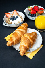 Fresh healthy breakfast with berries, oatmeal with yogurt, orange juice and French croissant with butter on a dark background. Healthy eating.