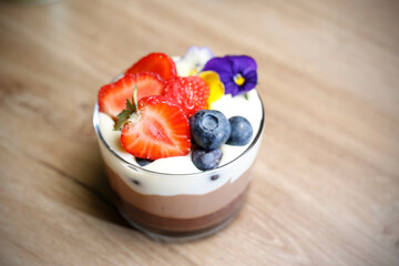 Chocolate mousse dessert in a glass cup decorated with fresh fruits, top view, selective focus, with blurred background.