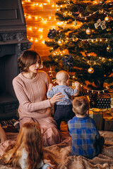 Obraz na płótnie Canvas Mother with children sitting by Christmas tree