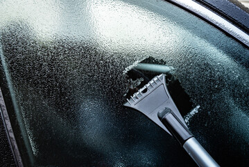 Cleaning of icy window on car with ice scraper on winter frosty morning.