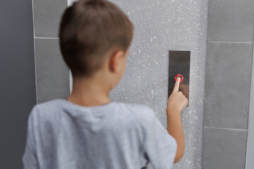 Boy tries to push the elevator button up and down. Child stretches out his hand and finger to press...