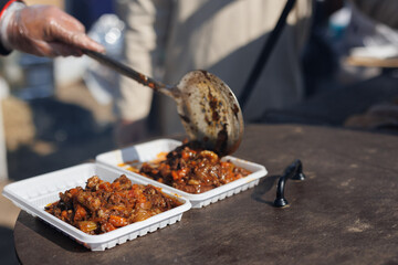 The cook puts a ladle of meat goulash from the cauldron into a picnic plate