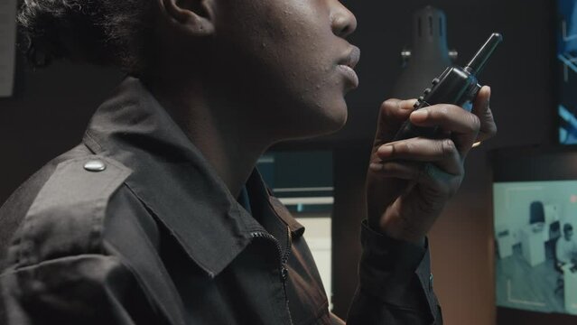 Tilt cropped shot of unrecognizable African American female security officer using handheld transceiver while controlling CCTV video footages on multiple monitors in guard room