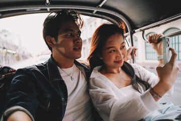 Happy and joyful Young Asian couple traveler tourists riding a tuk tuk tour, rickshaw style...