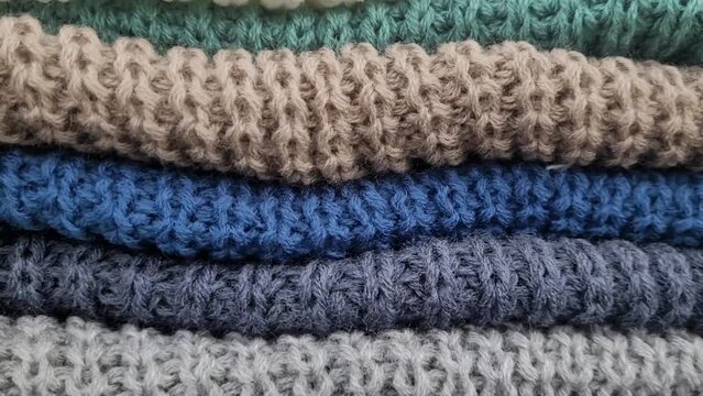 Bunch of knitted warm sweaters with different knitting patterns folded in stack. Fall winter season knitwear. Close up, copy space. High quality 4k footage