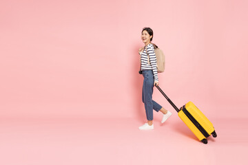 Happy young Asian woman traveler drag luggage isolated on pink background, Tourist girl having...
