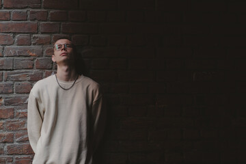 Young man in hoodie and jeans against a brick wall, light gradient.
