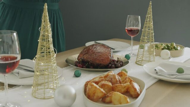Medium close-up 4k video of young African American woman putting dish with baked Christmas ham or gammon on dinner table served for Christmas eve. Festive season. Medium close-up with copy space.