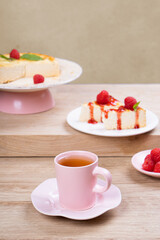 Colorful breakfast. Tea in a pink mug and dessert with raspberries on a light wooden table
