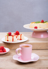 Colorful breakfast. Tea in a pink mug and dessert with raspberries on a light wooden table