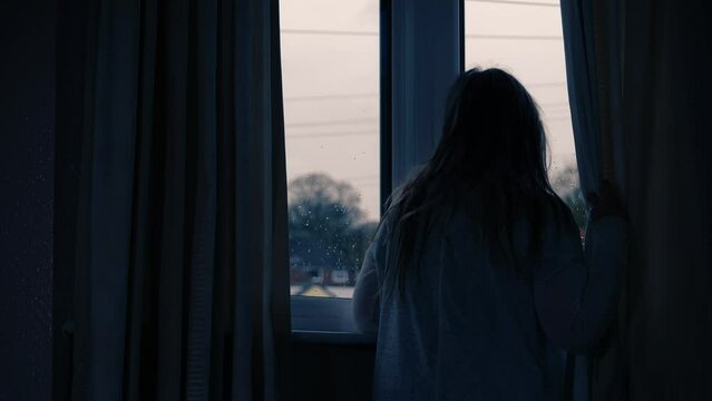 Woman Looking Out Of Window In Dark Room