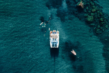 Drone view of Catamaran anchored in blue sea with swimming people in summer. Travel background....