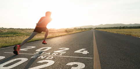 New year 2023 or start straight concept.word 2023 written on the asphalt road and athlete man runner stretching leg preparing for new year at sunset.Concept of challenge or career path and change. - obrazy, fototapety, plakaty