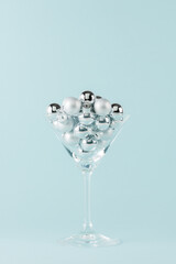 Martini glass with Christmas baubles on pastel blue background. Minimal Christmas theme. New Year party concept.