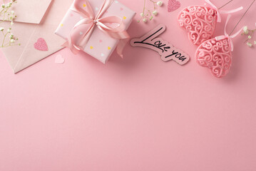 Celebrate love on Valentine's Day with this charming setup. Gift box, gypsophila, heart-shaped confetti, invitation envelope, and heart decor on sticks. Top view on pastel pink canvas with text space