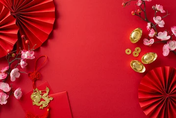 Foto op Plexiglas Dive into festive aura with top-view shot featuring fans, Feng Shui trinkets, traditional coins, sycee, envelopes, dragon charm wall hanging, sakura blossoms on red backdrop for text or promo content © ActionGP