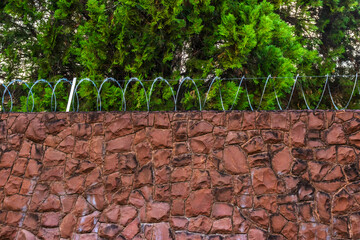 Stone wall with spiral-shaped steel fence with cutting blades, called concertina or popularly...