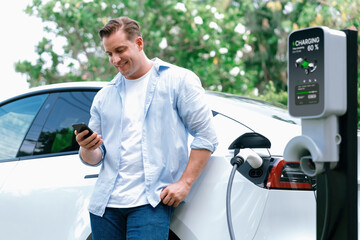 Modern eco-friendly man recharging electric vehicle from EV charging station, using Innovative EV...