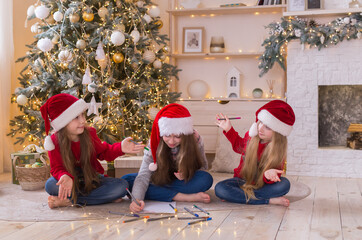 Three sisters write a letter to Santa. The girls are wearing beautiful Santa's helper hats. They...