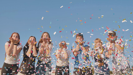 Friends blow colorful paper confetti on a sunny day.