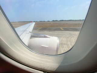 Looking through window aircraft during flight take off preparation with runway background. View from the airplane window. Daylight Sunny Bright during the day. Concept for traveling and solo trip.