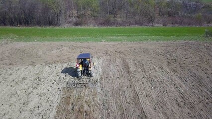 Obraz premium A farmer on a tractor with a seeder sows grain in plowed land in a private field in the village area. Mechanization of spring field work. Farmer's everyday life. Processing of land. The agrarian
