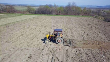 A farmer on a tractor with a seeder sows grain in plowed land in a private field in the village area. Mechanization of spring field work. Farmer's everyday life. Processing of land. The agrarian