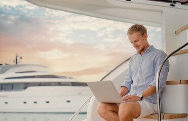 Luxury traveling and working. Handsome young man using laptop on the deck of modern yacht. - Powered by Adobe
