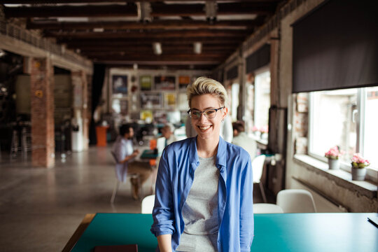 Smiling young woman in startup office looking at camera