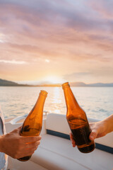 Party with friends. Close up of two male hands holding bottles of beer on the yacht sailing the sea.