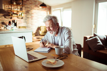 Senior man working at home with laptop and papers on desk