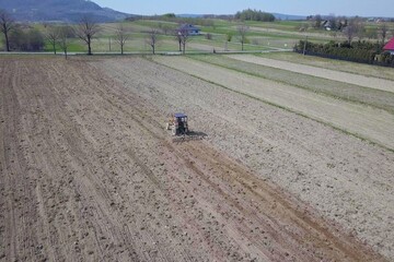 A farmer on a red tractor with a seeder sows grain in plowed land in a private field in the village area. Mechanization of spring field work. Farmer's everyday life. Processing of land. The agrarian.